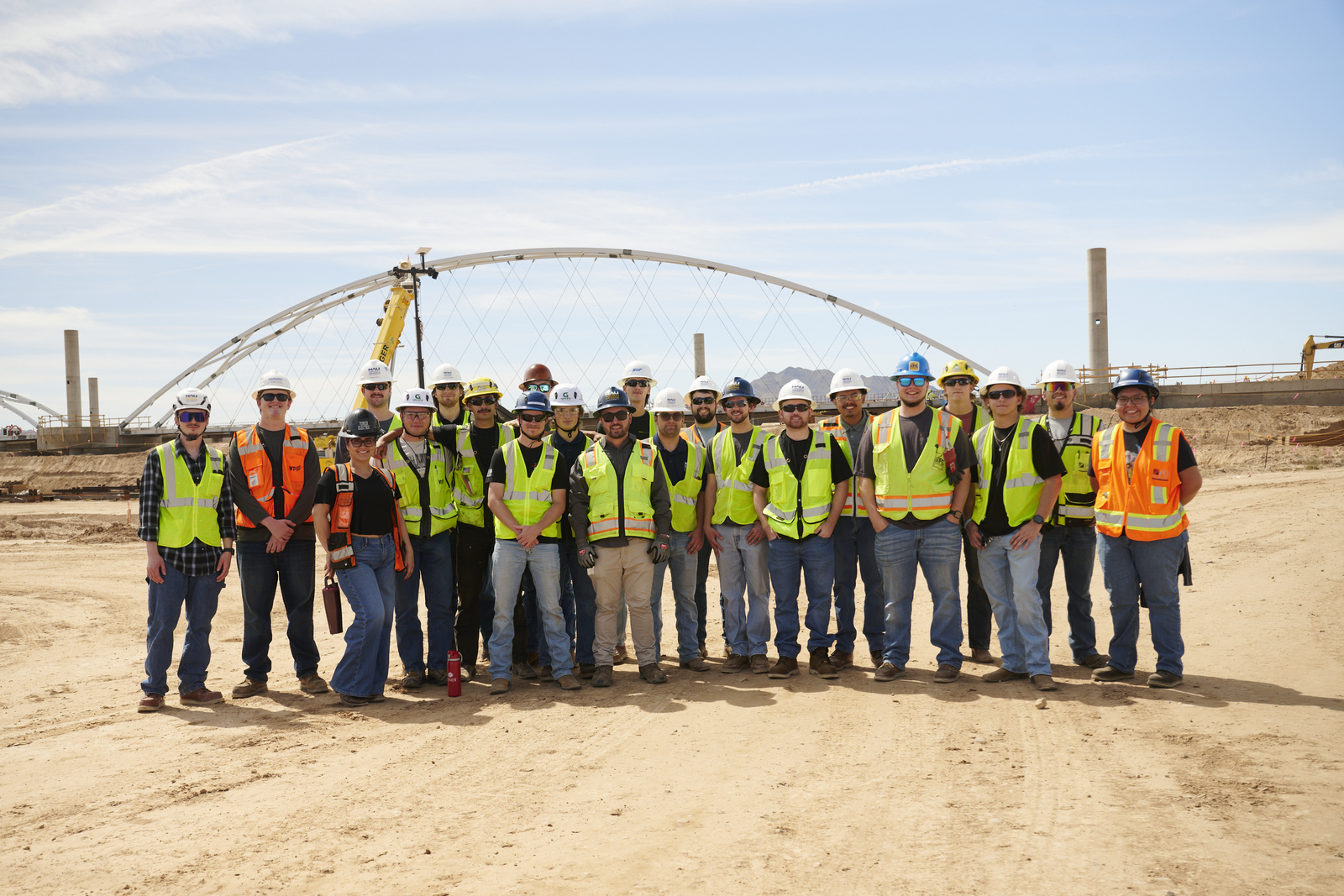 A group of NAU students in hard hats and reflective vests pose at a construction site.