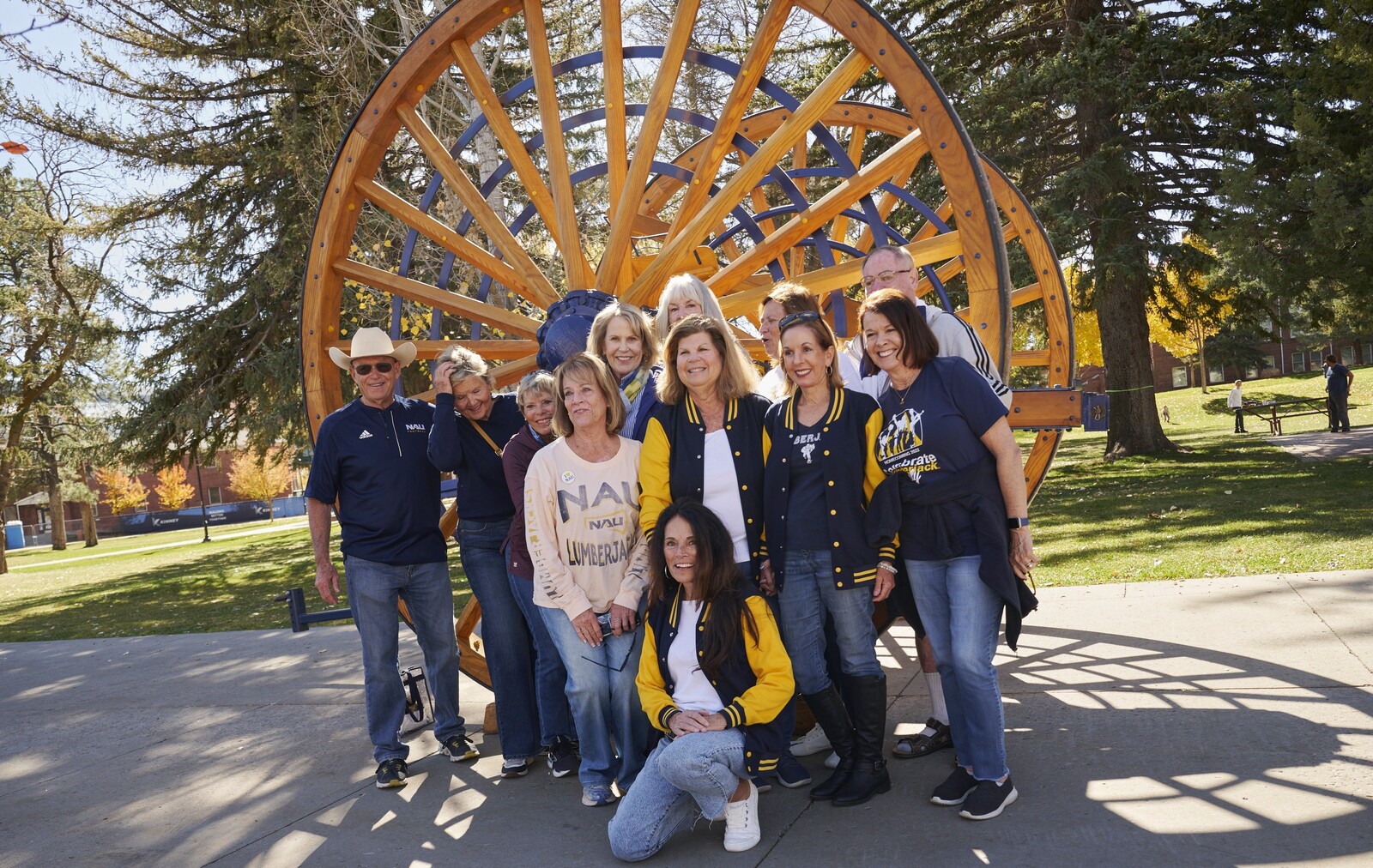 A group of NAU alumni pose in front of a wagon wheel for Homecoming
